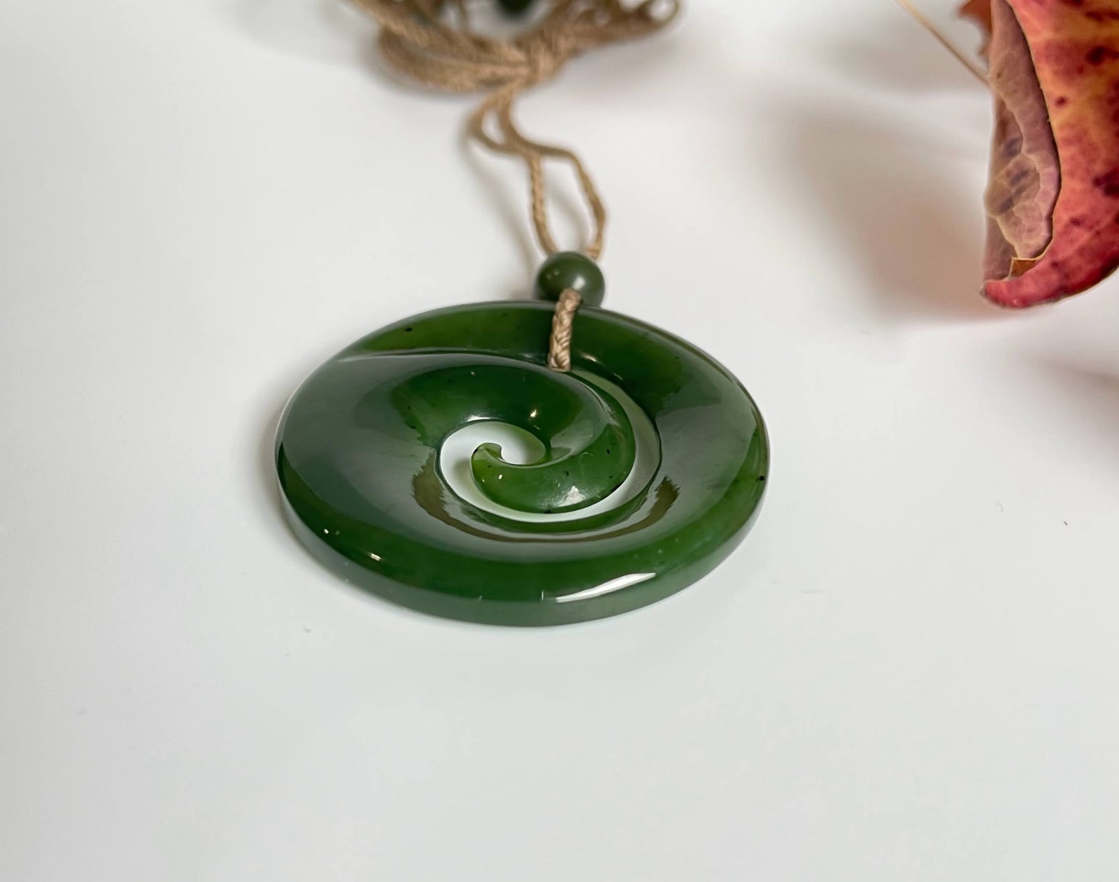 Green jade koru pendant with a spiral design on a natural cord with a bead above