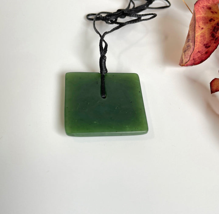 Green jade square pendant with satin finish on a black cord necklace