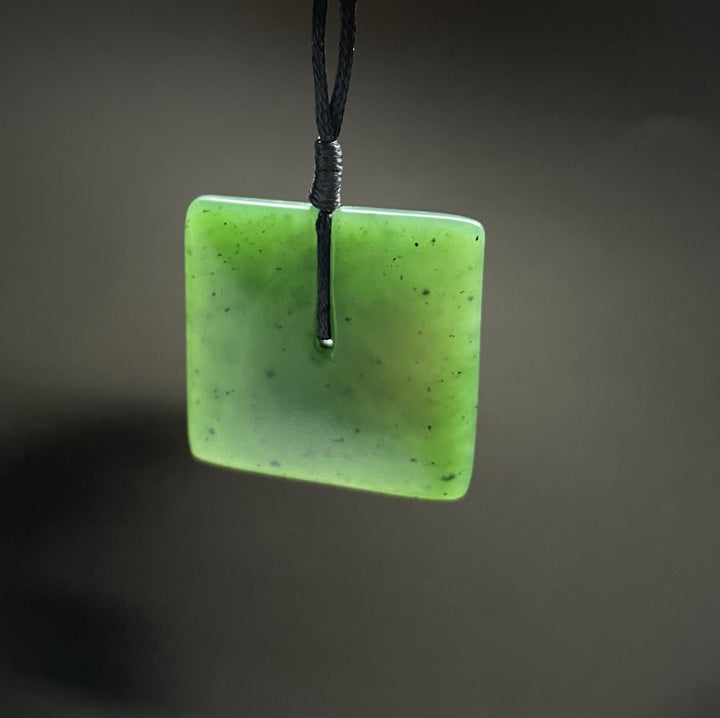 Close-up of a square green jade pendant with satin finish threaded on a black cord