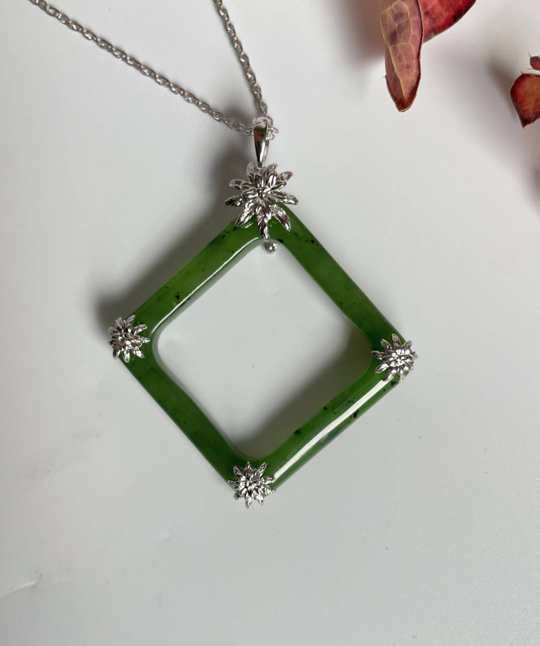 Green jade square pendant with four silver flower end caps on a silver chain