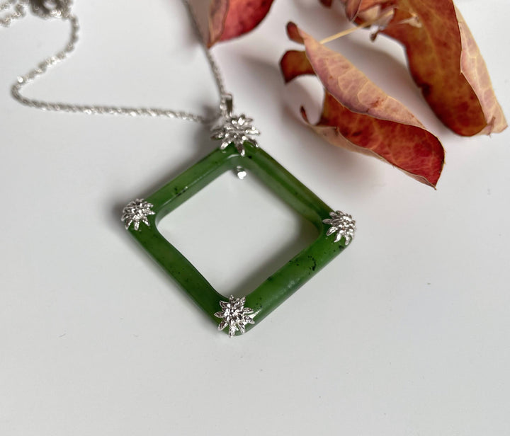 Close up of jade square pendant showing silver floral accents at each corner on a silver chain