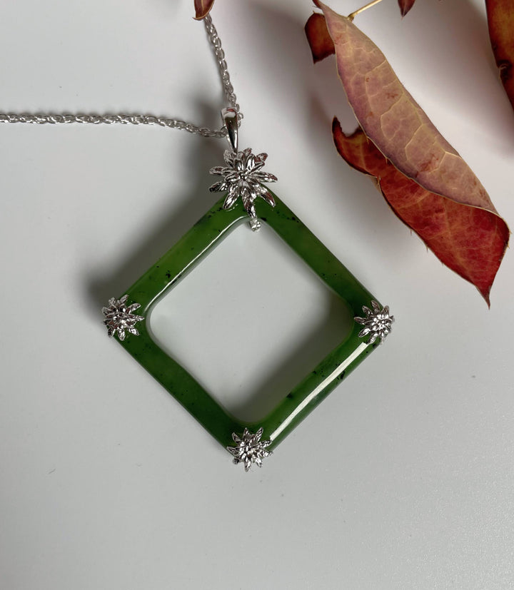 Green jade square pendant with hollow center in a silver frame and four silver floral accents at the corners on a silver chain