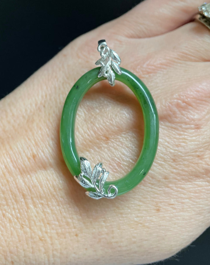 Jade green oval pendant with silver leaf accents worn on a finger.