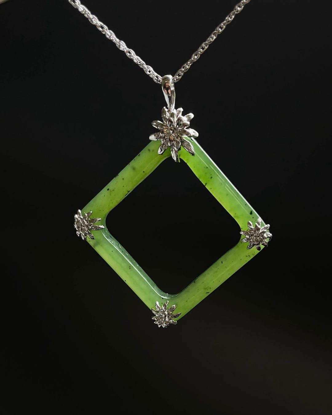 Green jade square pendant with hollow center framed in silver and silver flower accents at each corner on a chain