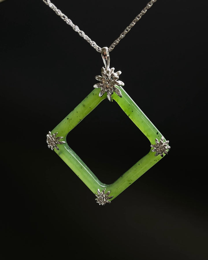 Green jade square pendant with hollow center framed in silver and silver flower accents at each corner on a chain