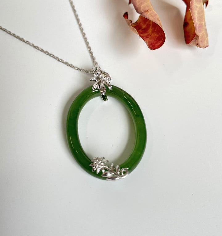 Jade oval pendant with silver leaf and floral accents on a delicate chain