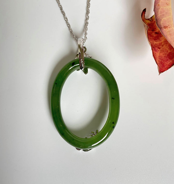 Jade oval pendant featuring top leaf bail and bottom floral detail on a silver chain