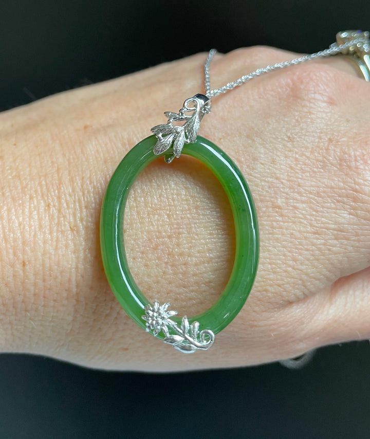 Jade green oval pendant on a silver chain worn on the wrist, featuring leaf and floral silver accents.