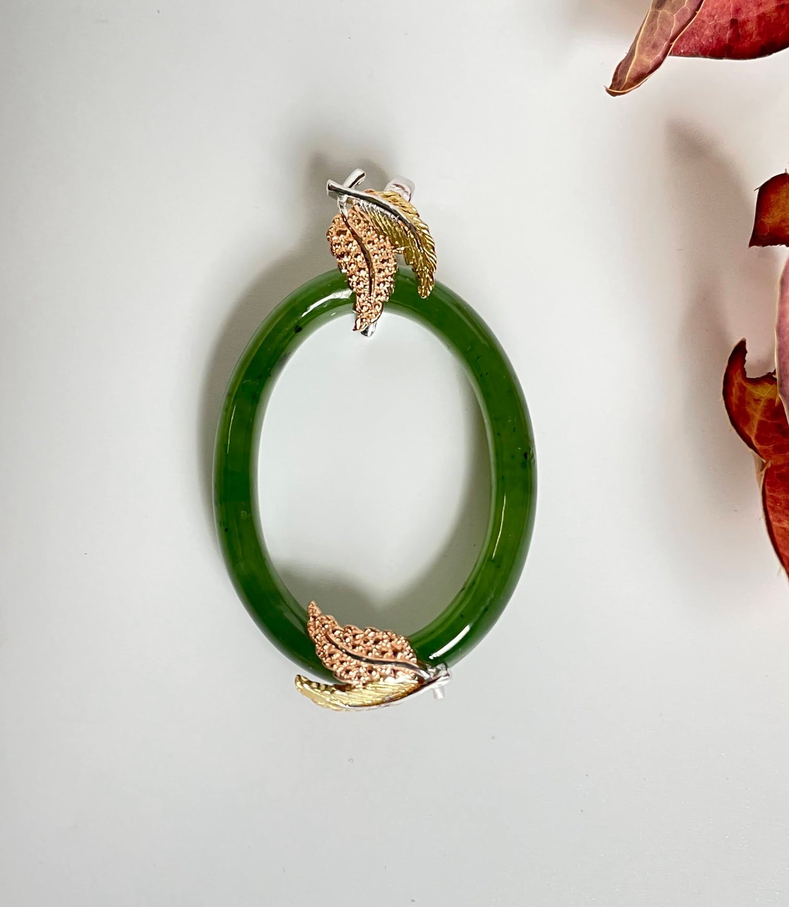 Jade green oval pendant with gold and silver leaf accents at top and bottom.