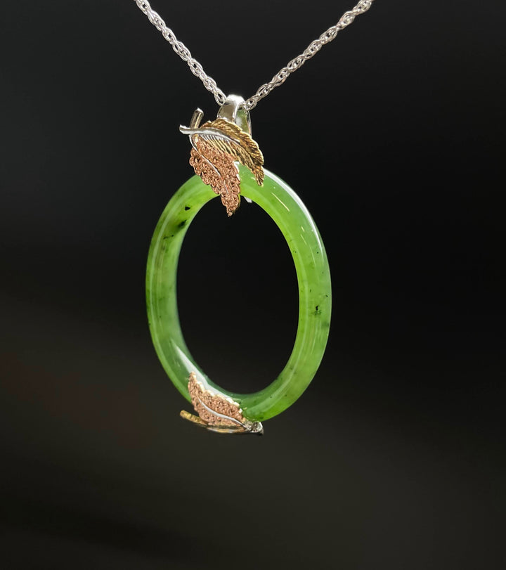 Green jade oval pendant with gold and copper leaf accents on a silver chain.