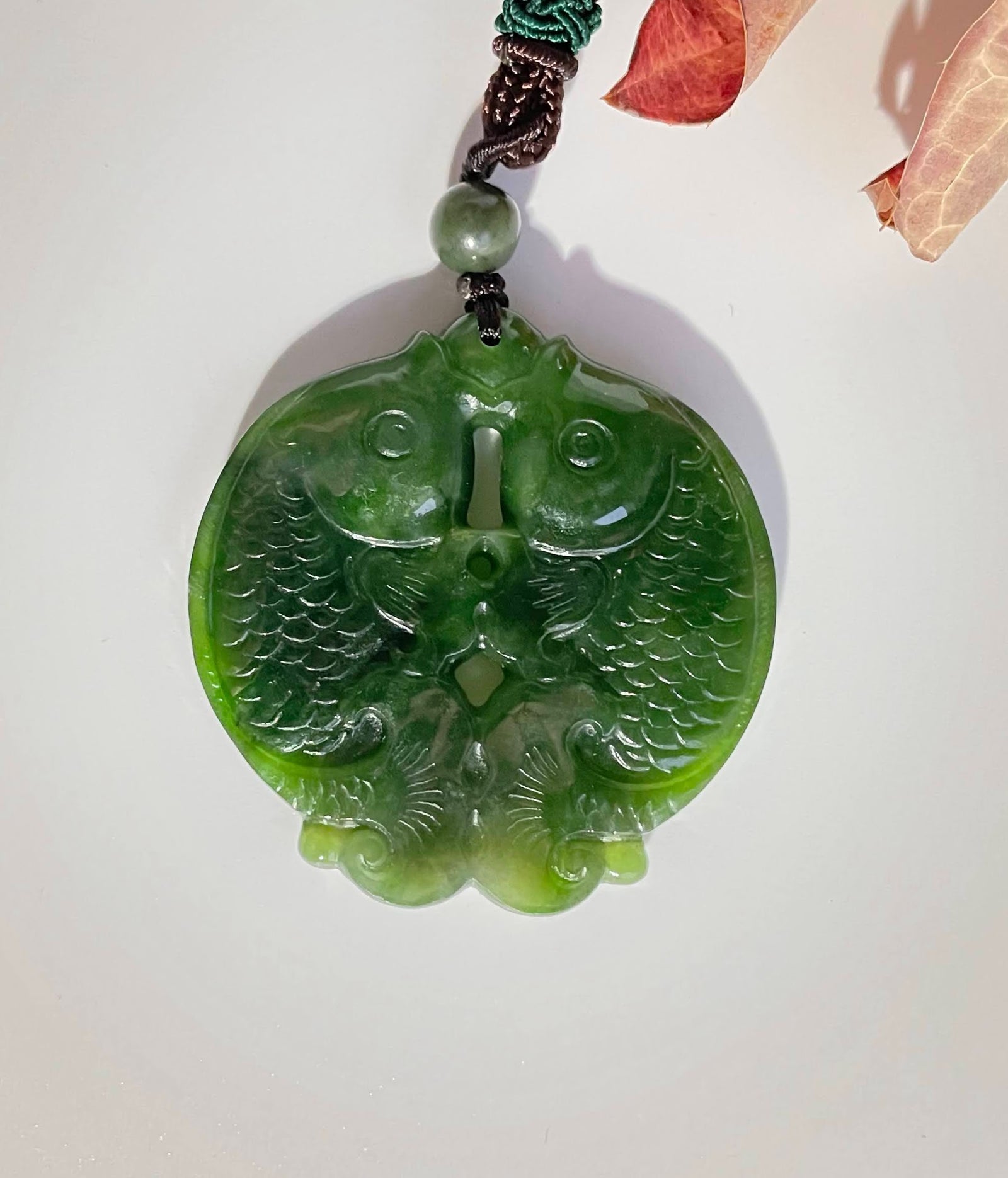 Green jade double koi fish pendant with carved detailing hanging from a cord.