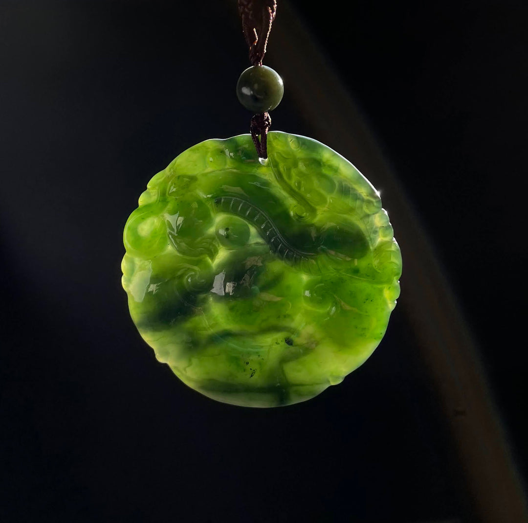 Double sided dragon pendant carved from green jade on a brown cord