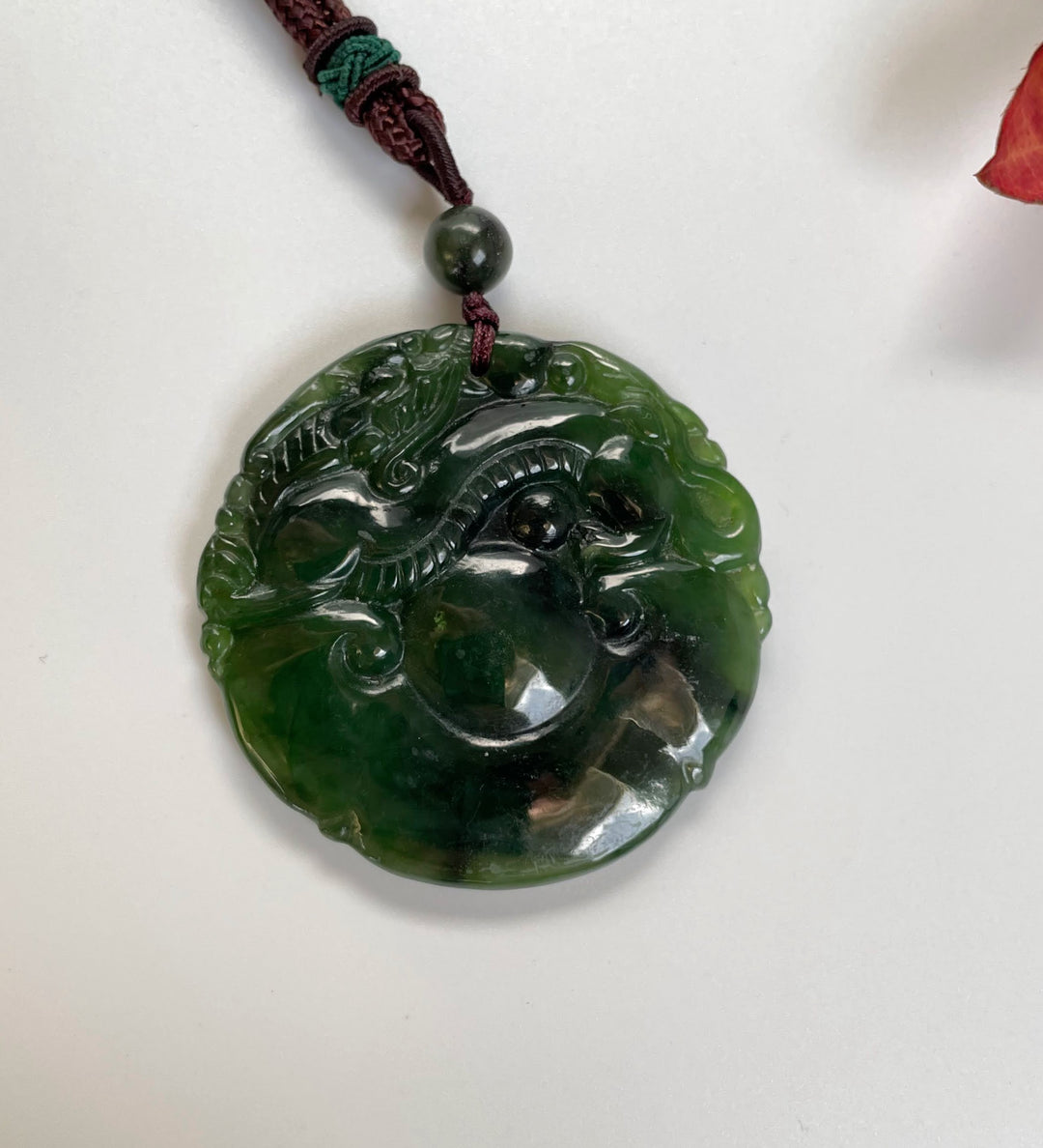 Green jade disc pendant with dragon relief carved along its edge suspended from a braided cord.