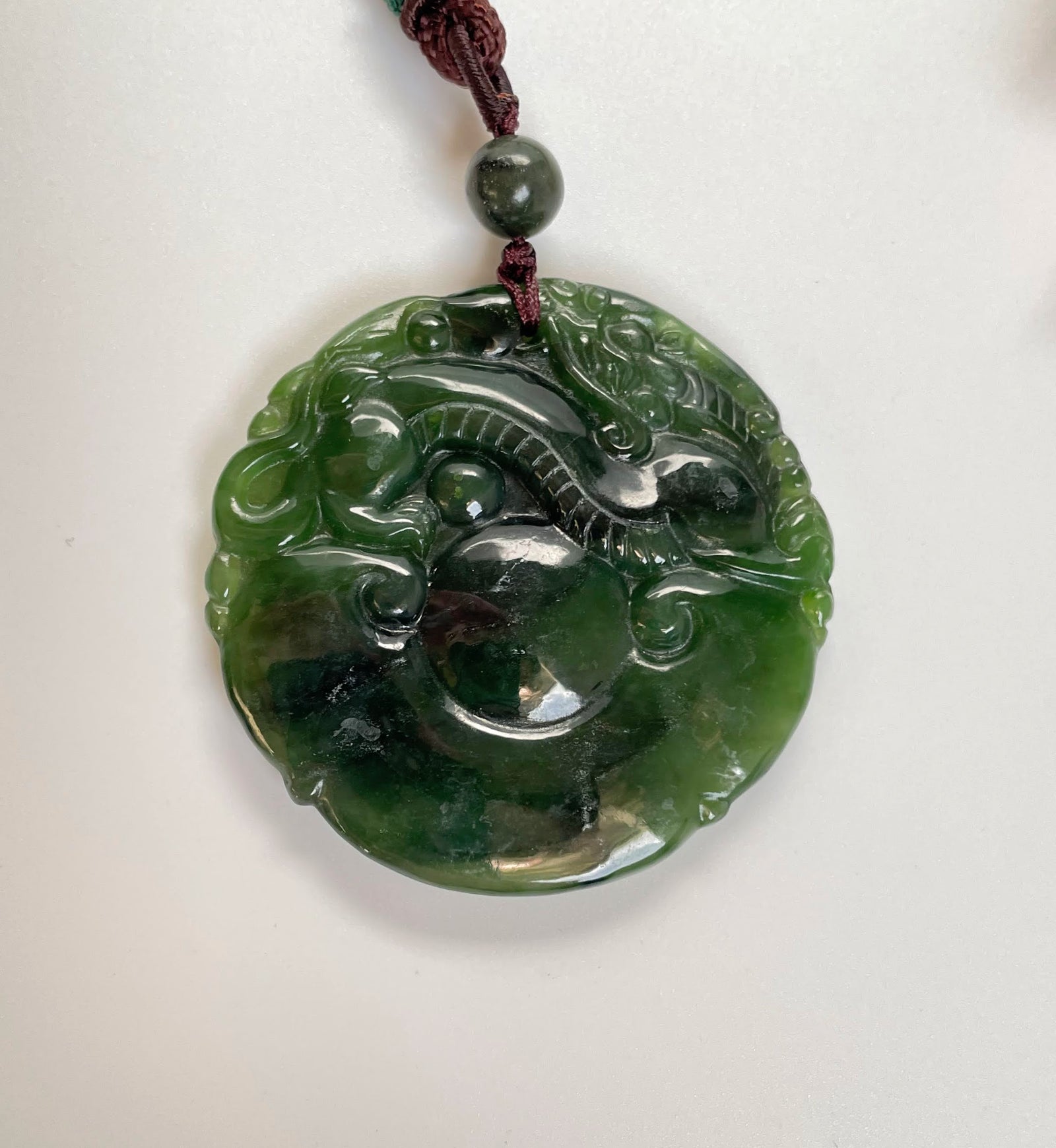 Double sided dragon pendant 50mm carved from green jade circular disc on a burgundy cord.