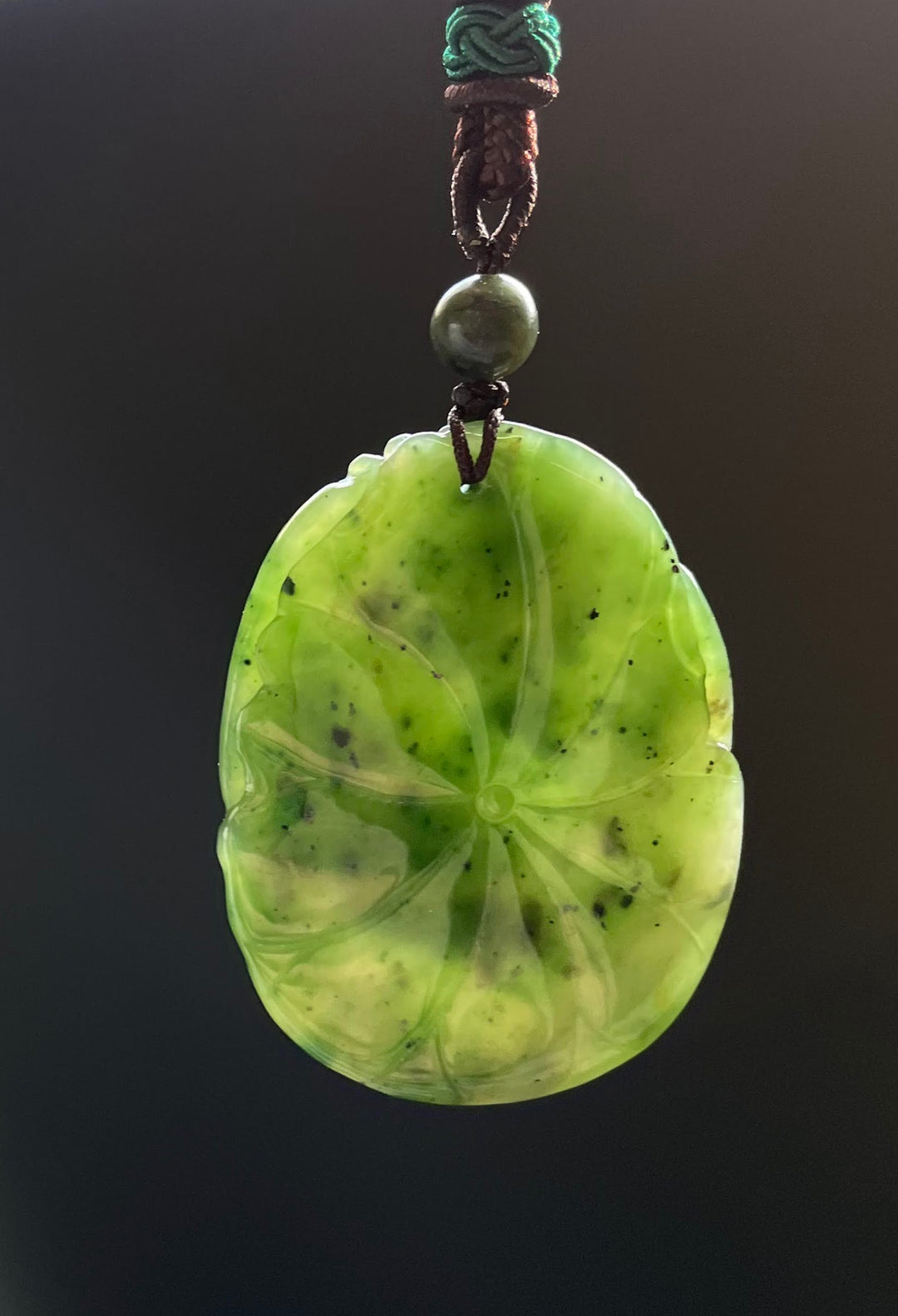 Lime green circular jade pendant with radiating petal lines, suspended from a braided brown cord with a green bead above