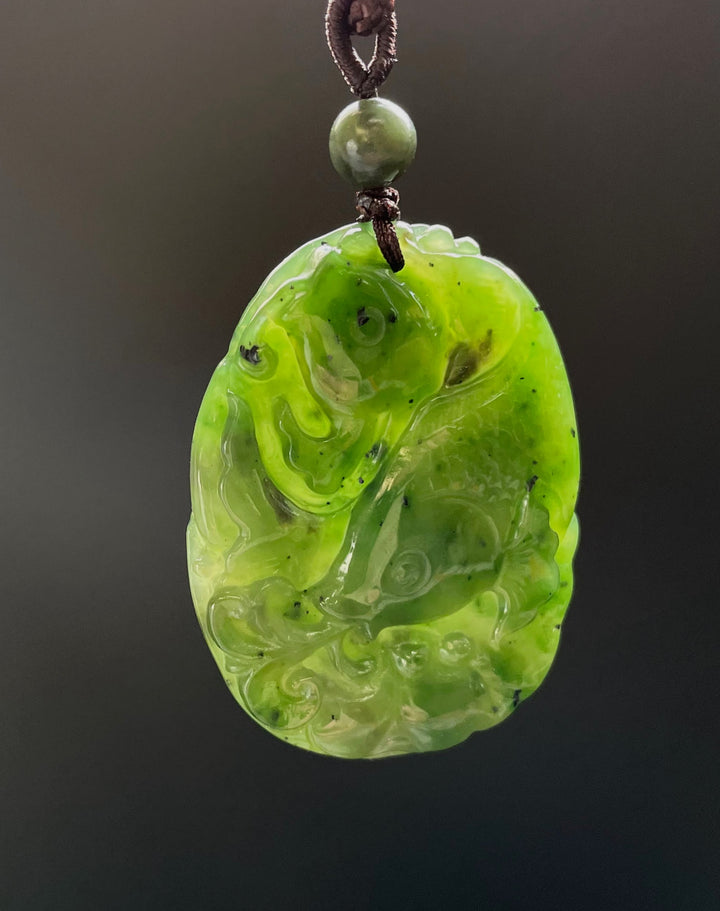Bright neon green jade koi fish pendant with swirling carving hanging from a brown cord with a green bead above