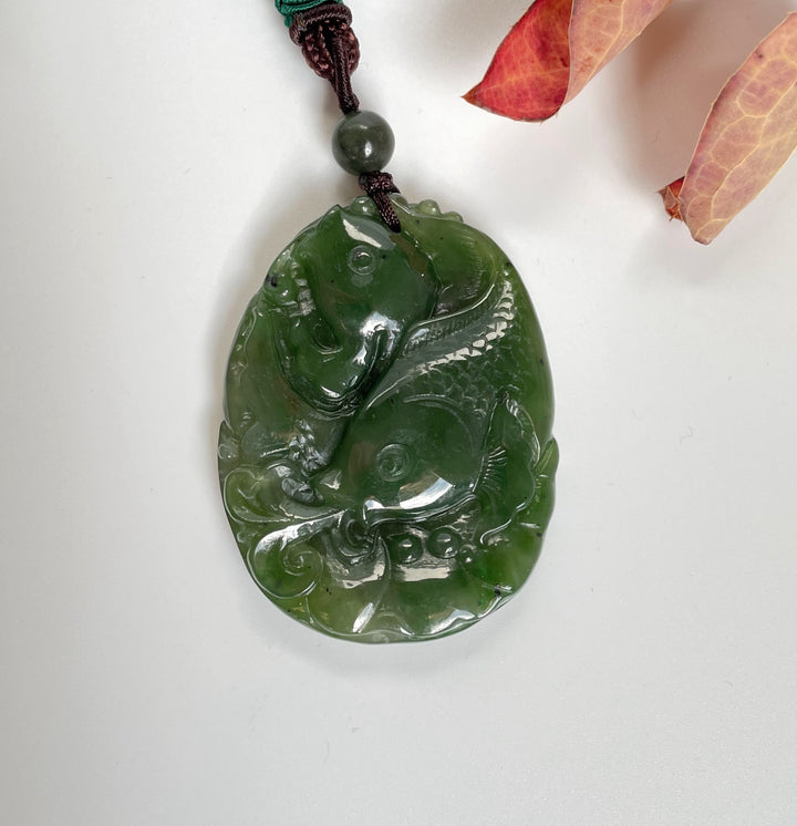 Jade koi fish pendant in deep green carved with two fish on a braided cord with a green bead