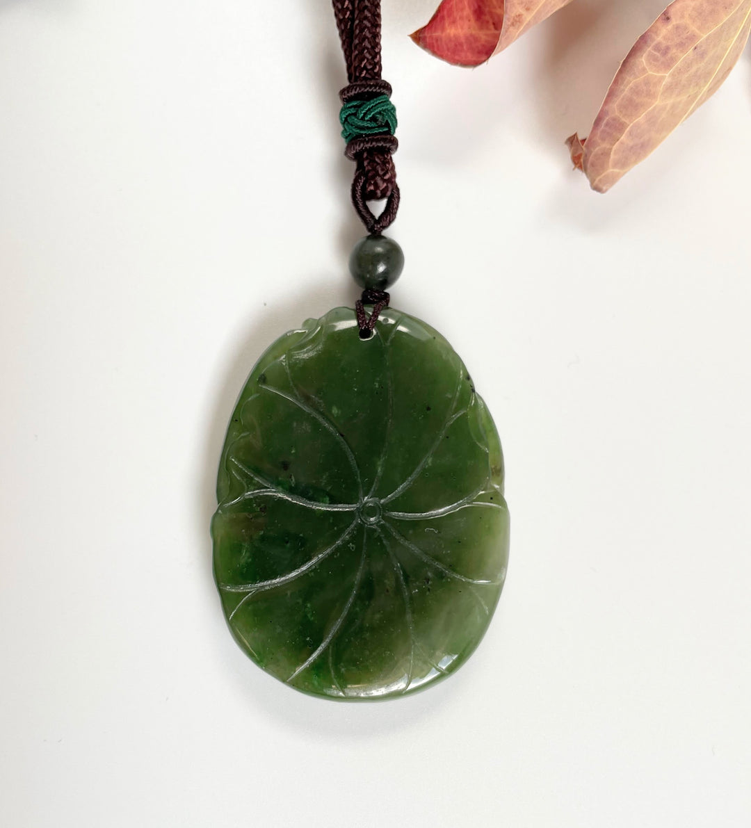 Leaf shaped jade pendant with carved vein pattern on a brown cord with a green bead above