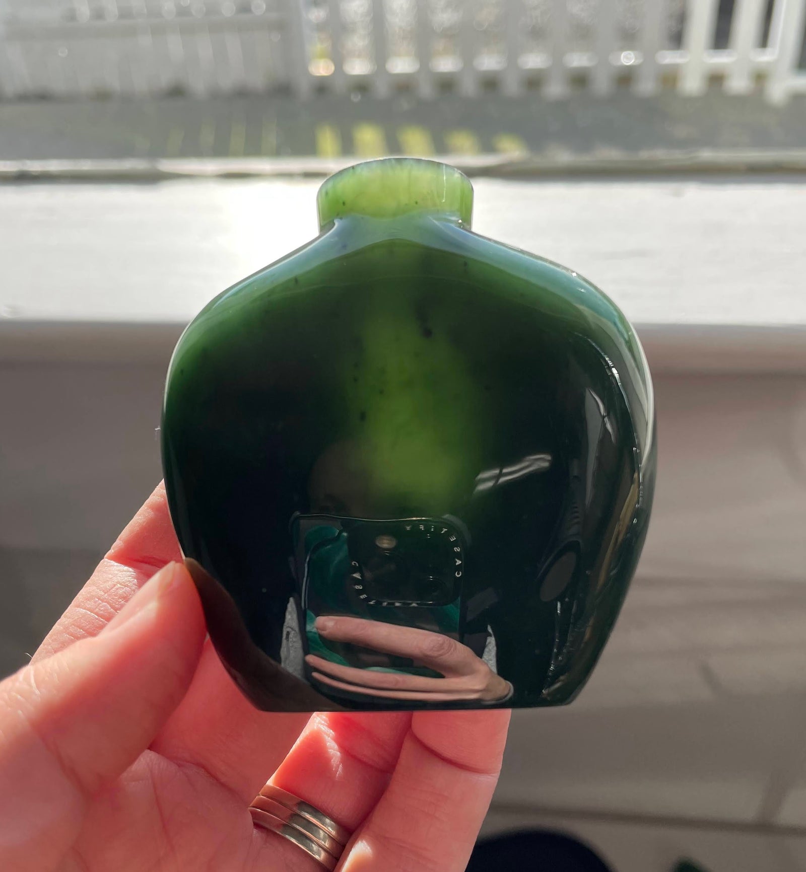 Dark green glass perfume bottle with rounded square shape held in hand