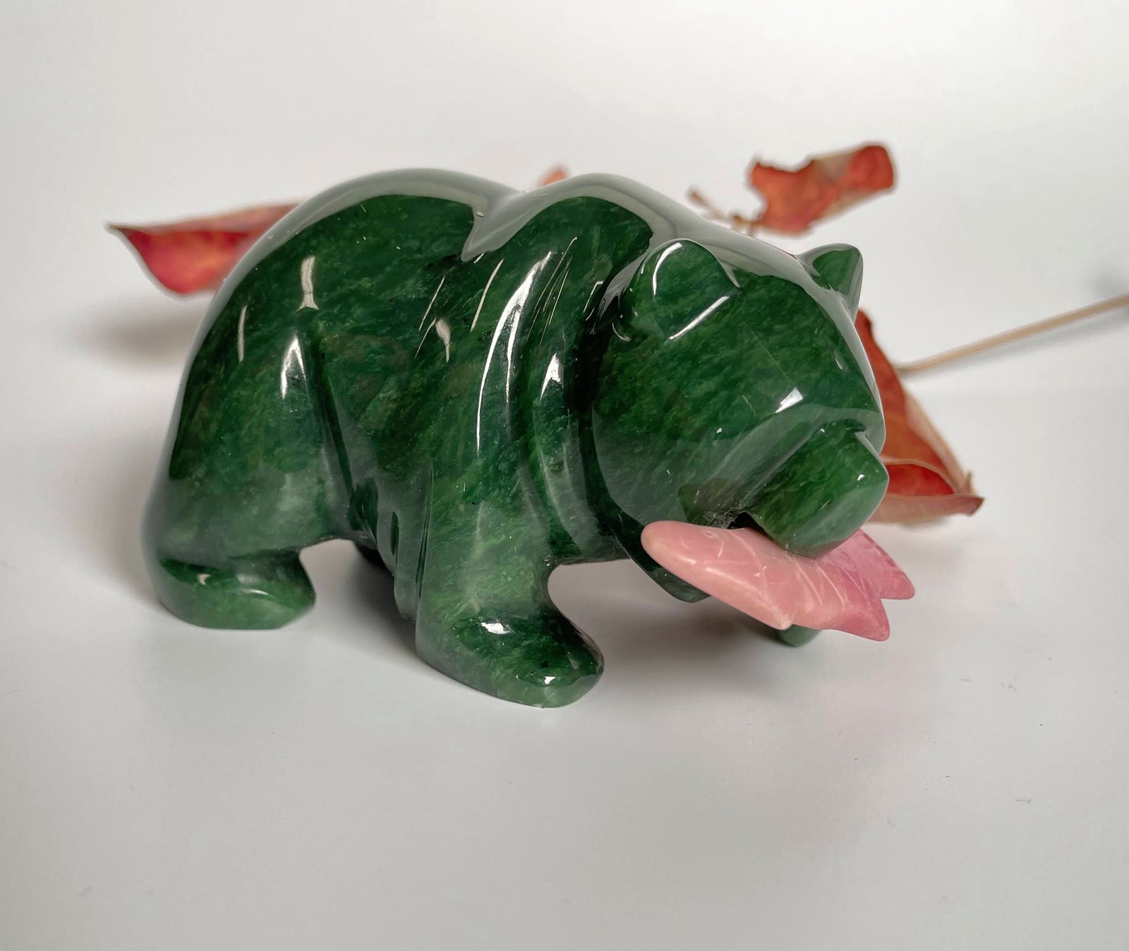 Green jade bear with pink rhodonite fish in its mouth, shown from the side.