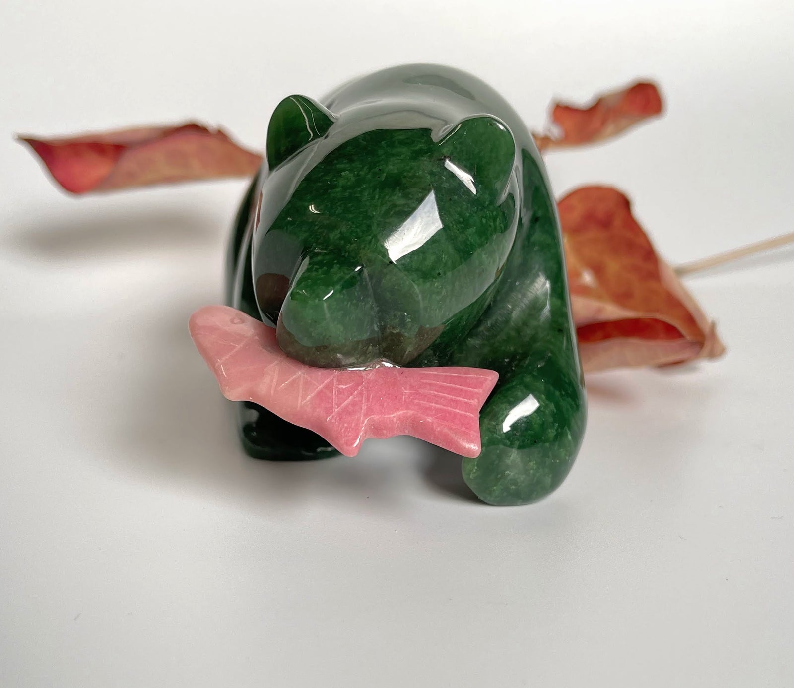 Green jade bear with pink rhodonite fish in its mouth, shown from a front-left angle.