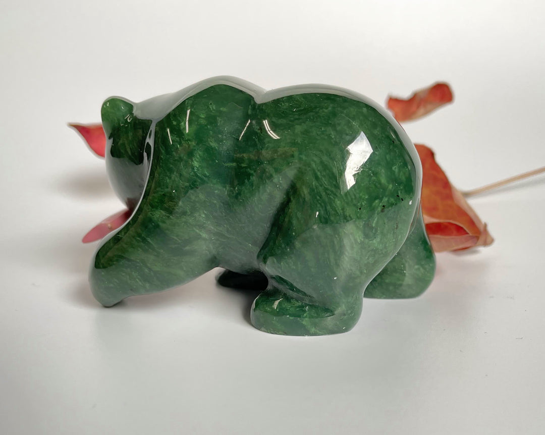 Side view of a dark green jade bear with a pink rhodonite fish in its mouth against a white background