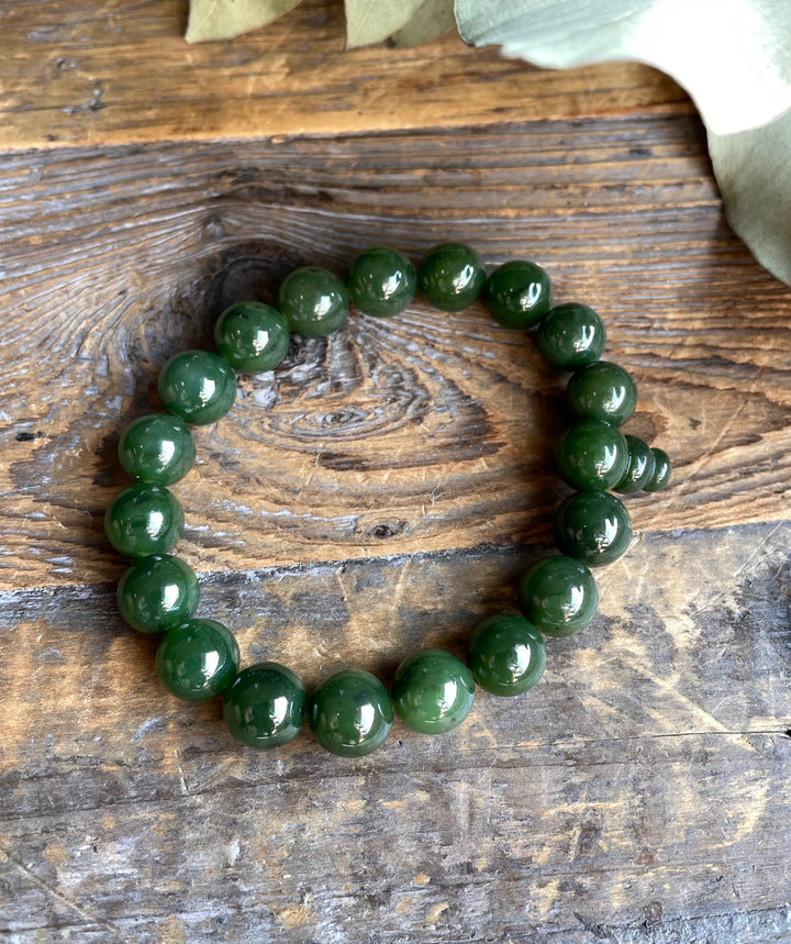 Single strand green bead mala bracelet arranged in a circle on a rustic wooden surface.