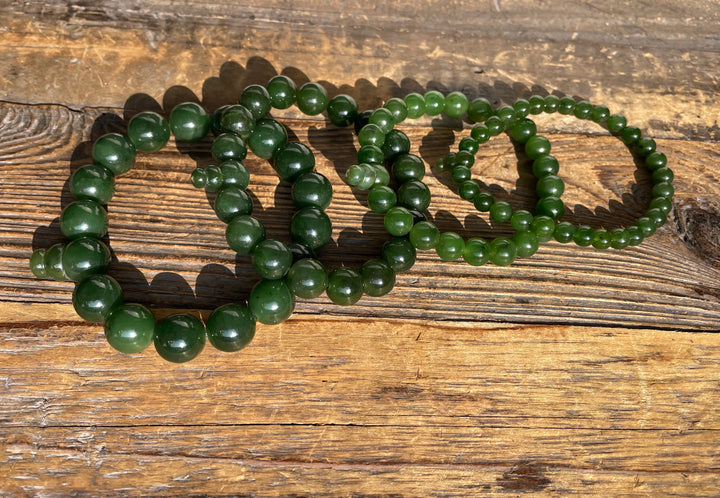 Dark and light green mala bracelets with large beads arranged on a wooden surface.