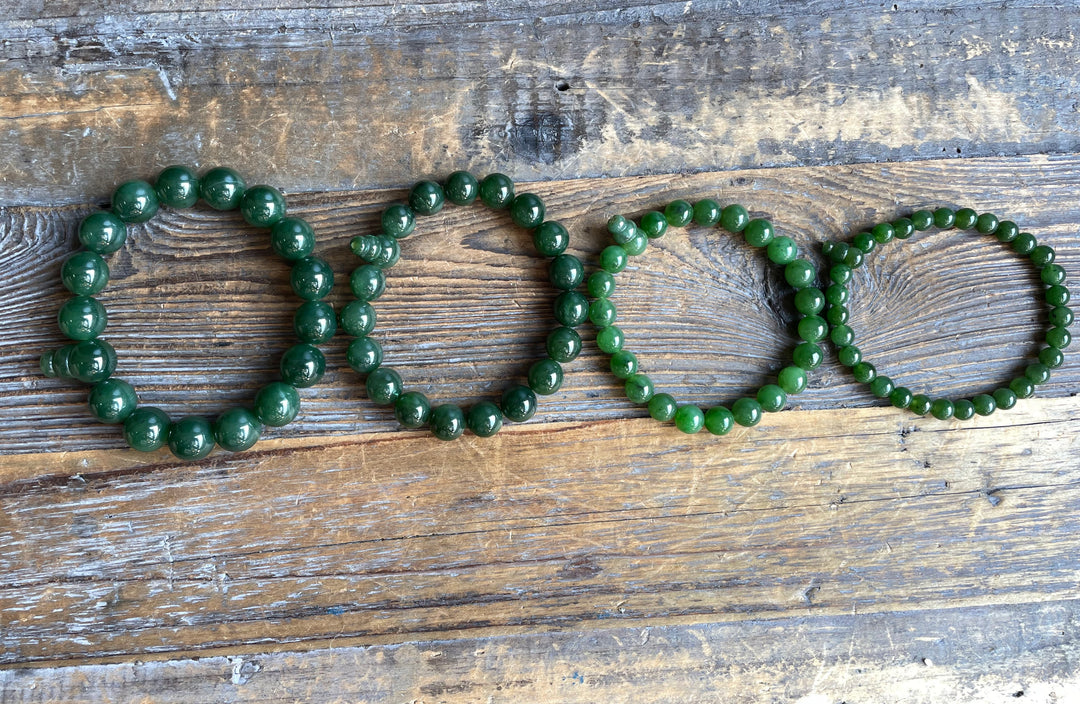 Green mala bracelets of varying bead sizes laid across a weathered wooden surface.