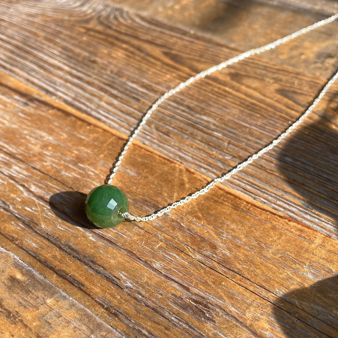 12mm faceted jade bead pendant on a silver chain resting on a wooden surface