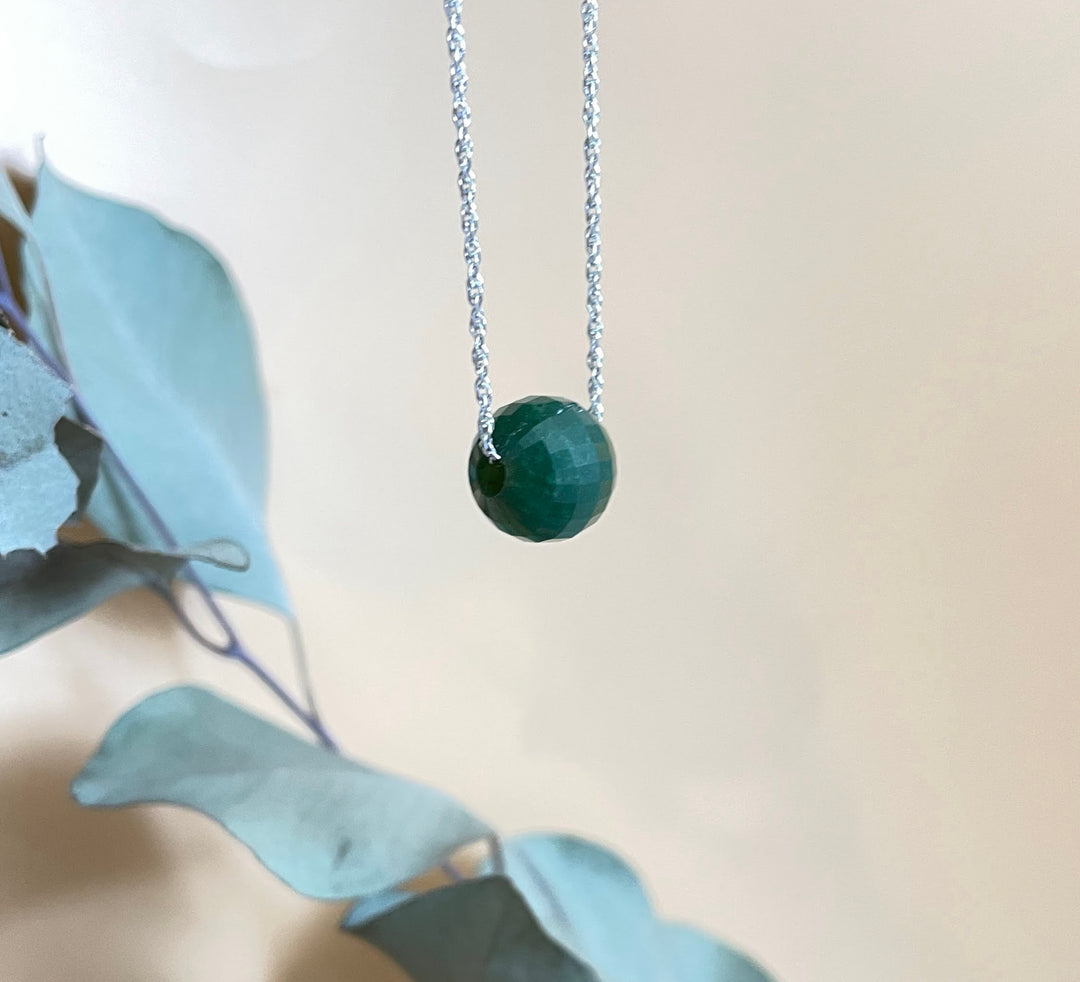 Green faceted jade bead pendant on a silver chain hanging against a pale backdrop.