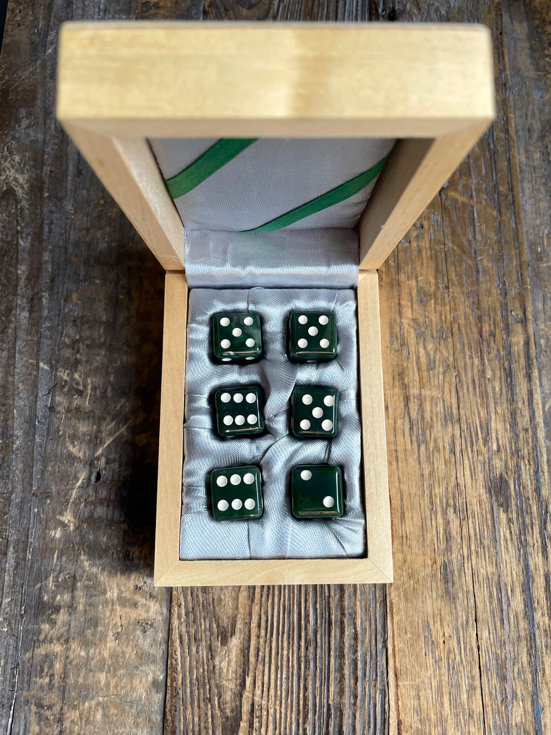 Open wooden dice case with six dark green dice resting on a pale satin lining.