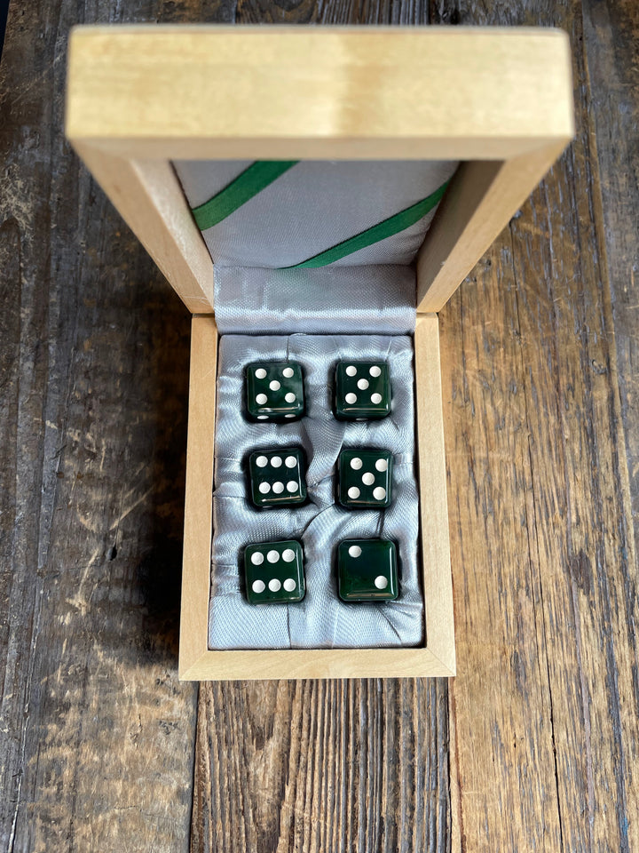Open wooden dice case with six dark green dice resting on a pale satin lining.