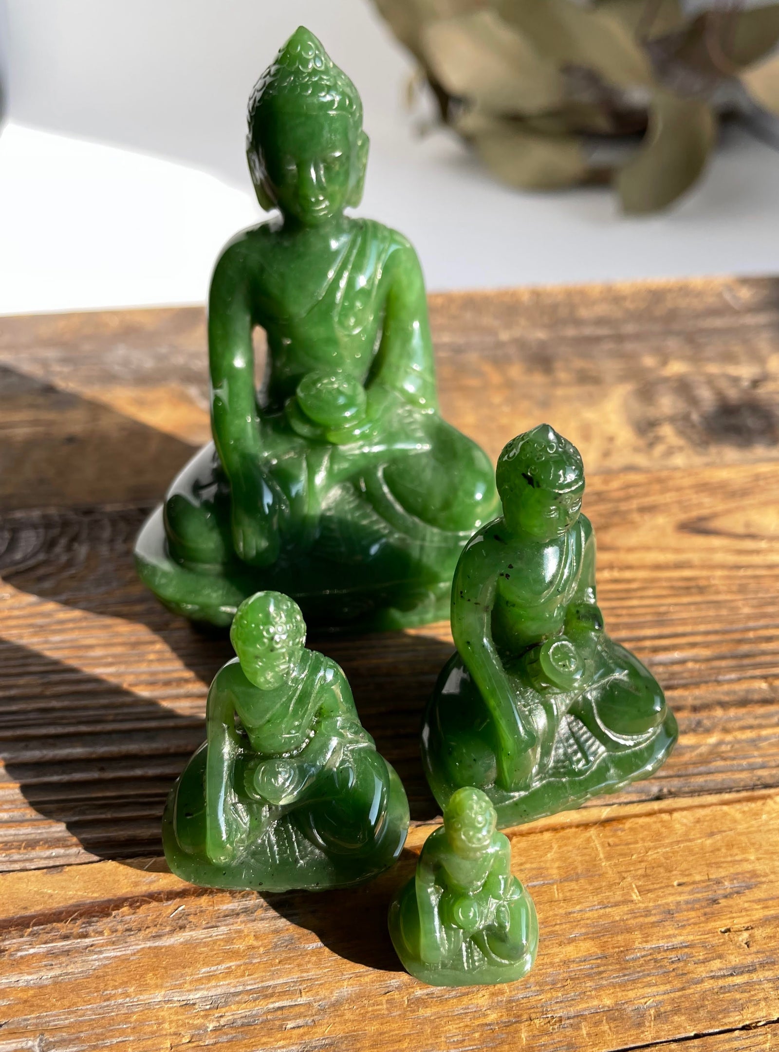 Group of three green jade Buddha statues in varying sizes displayed on a wooden surface.