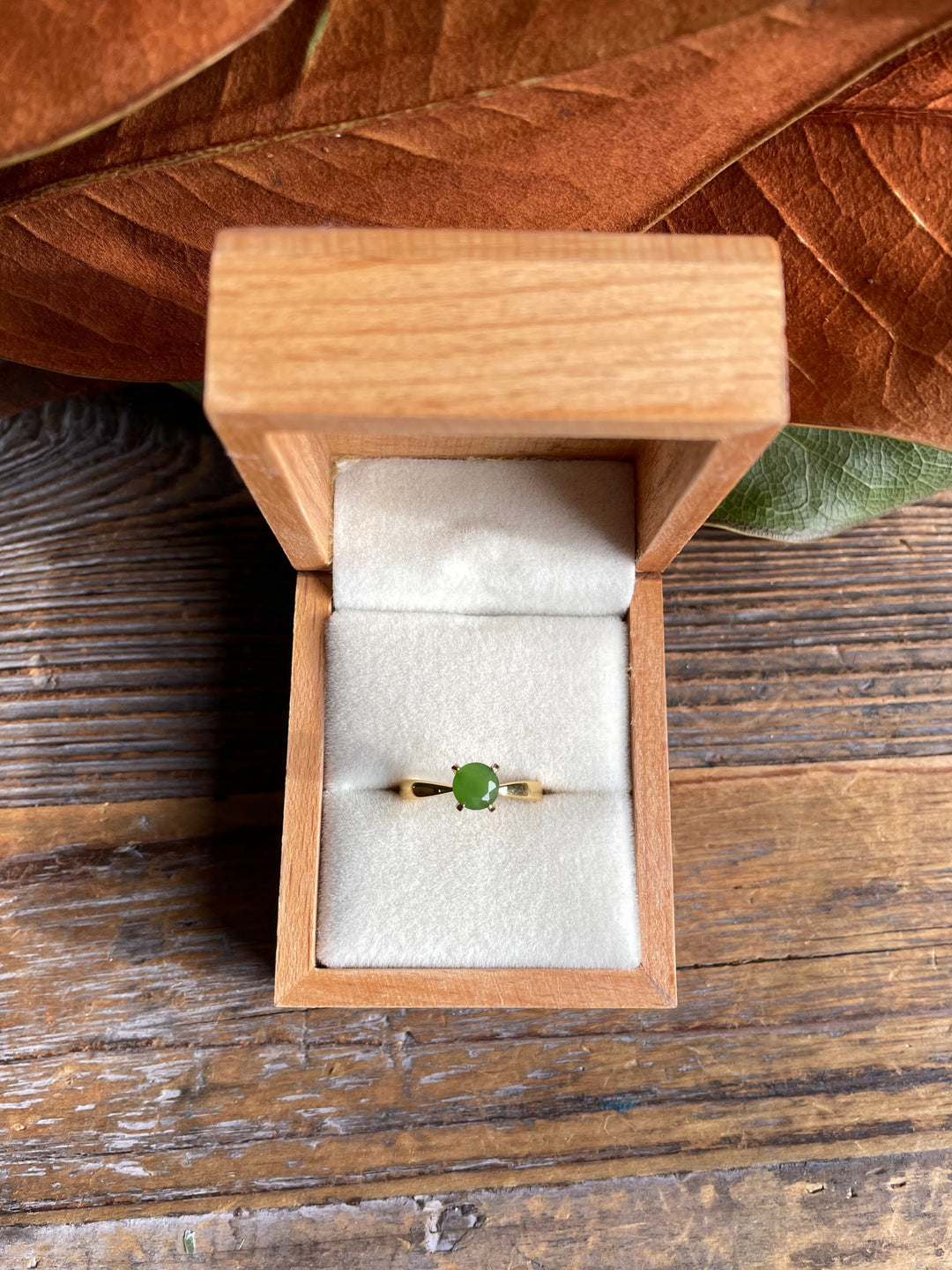 Green jade ring with a gold band in an open wooden jewelry box