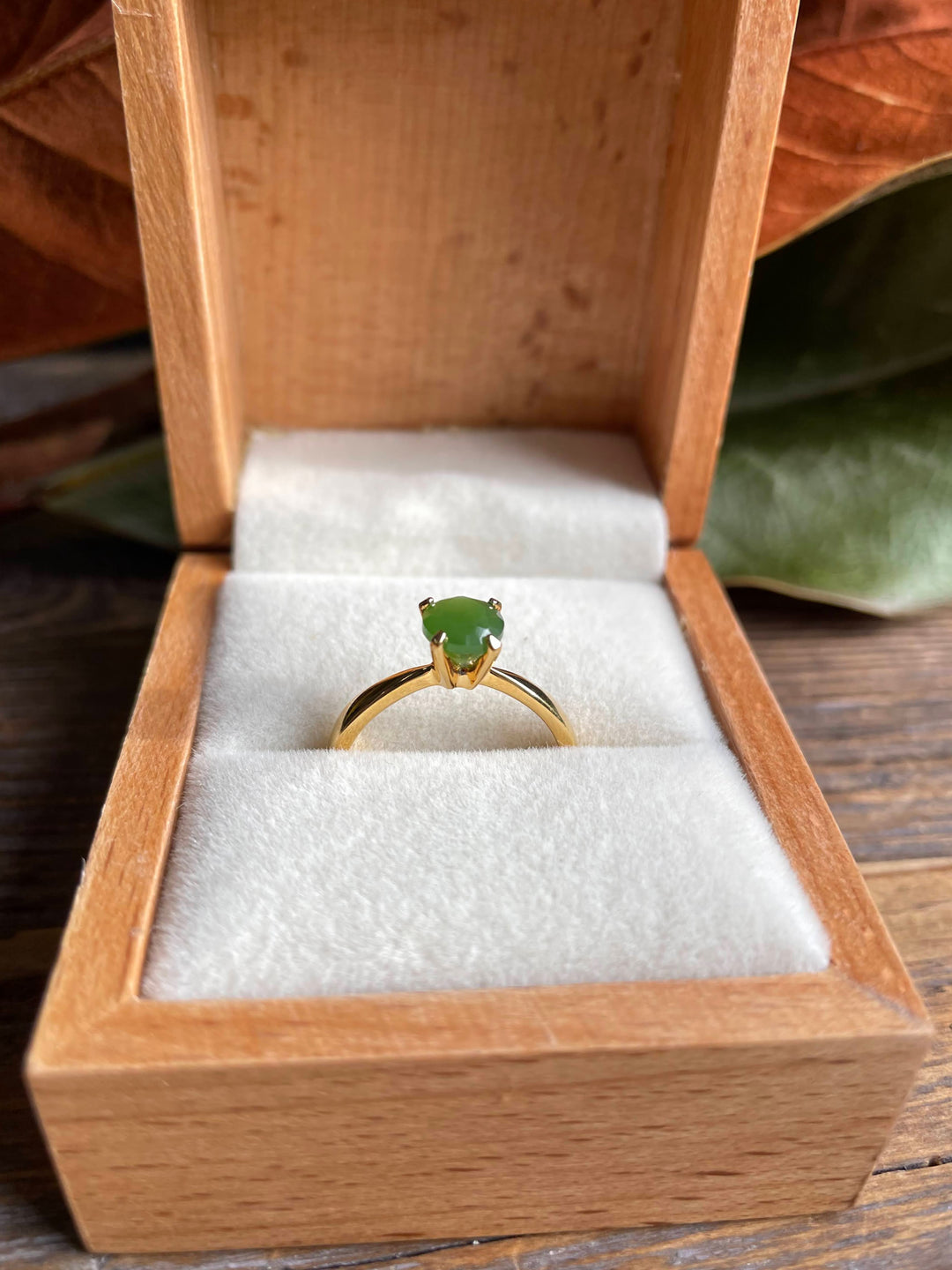Green jade ring in an open wooden box with white velvet lining