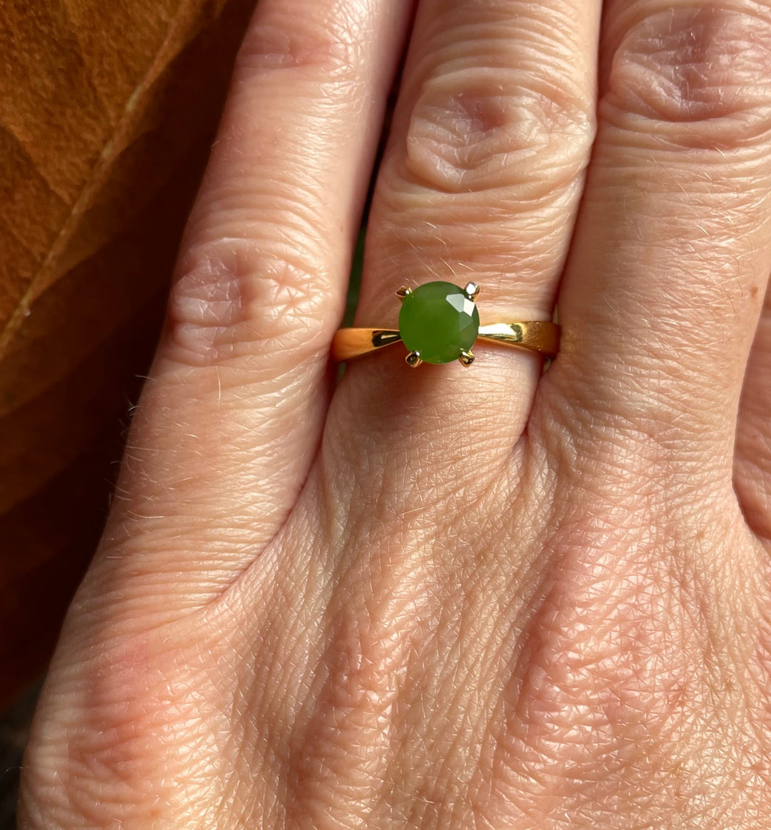 Green jade faceted ring on a gold band worn on a finger