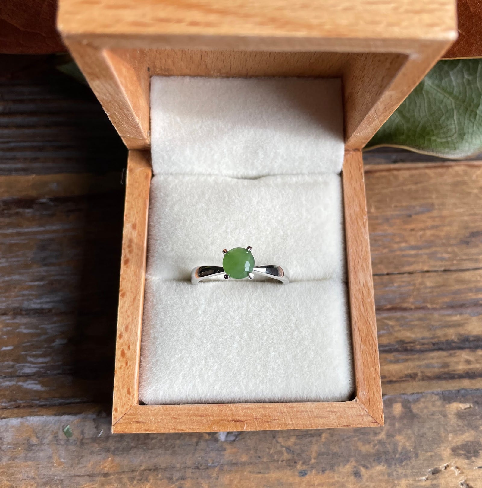 Open wooden box shows a green jade ring set in a silver band on white velvet