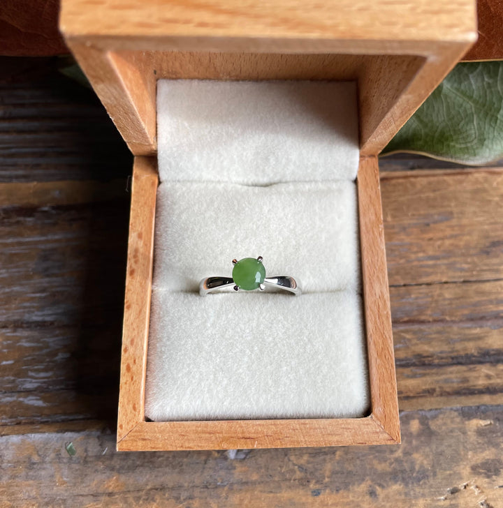 Open wooden box shows a green jade ring set in a silver band on white velvet