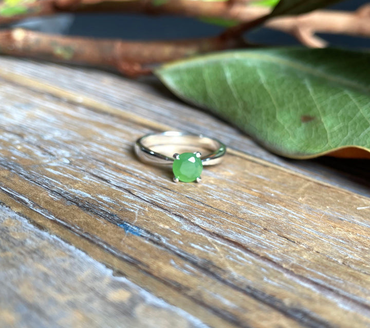 Green jade ring with a silver band resting on a rustic wooden surface