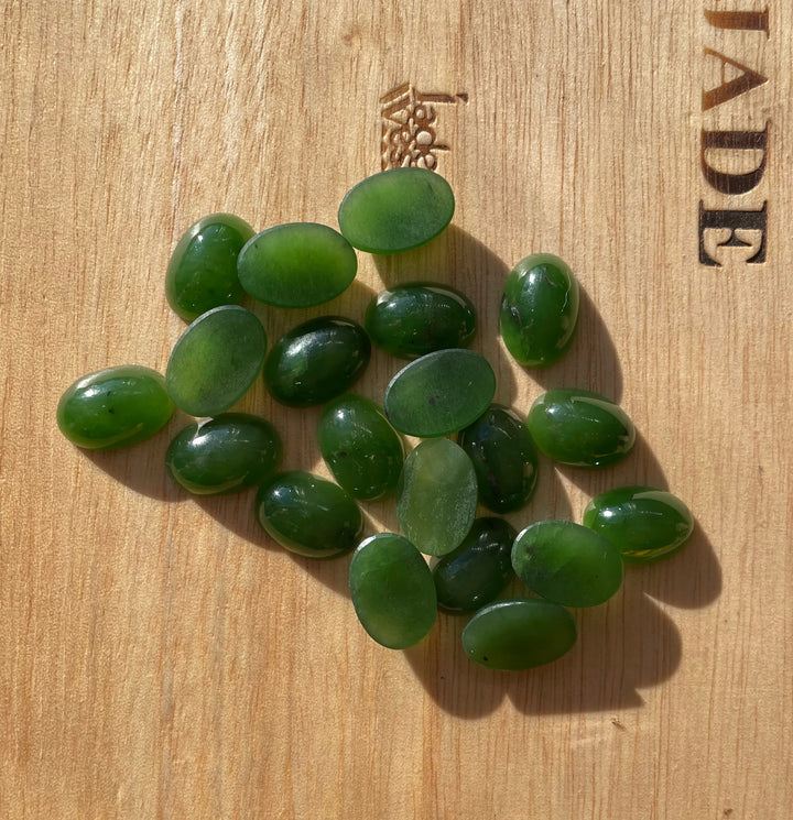 Group of 14x10mm rich green oval Siberian jade cabochons on wood surface