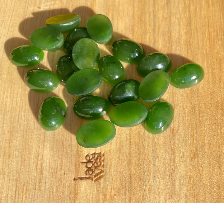 Rich green Siberian jade oval cabochons scattered on a wooden surface