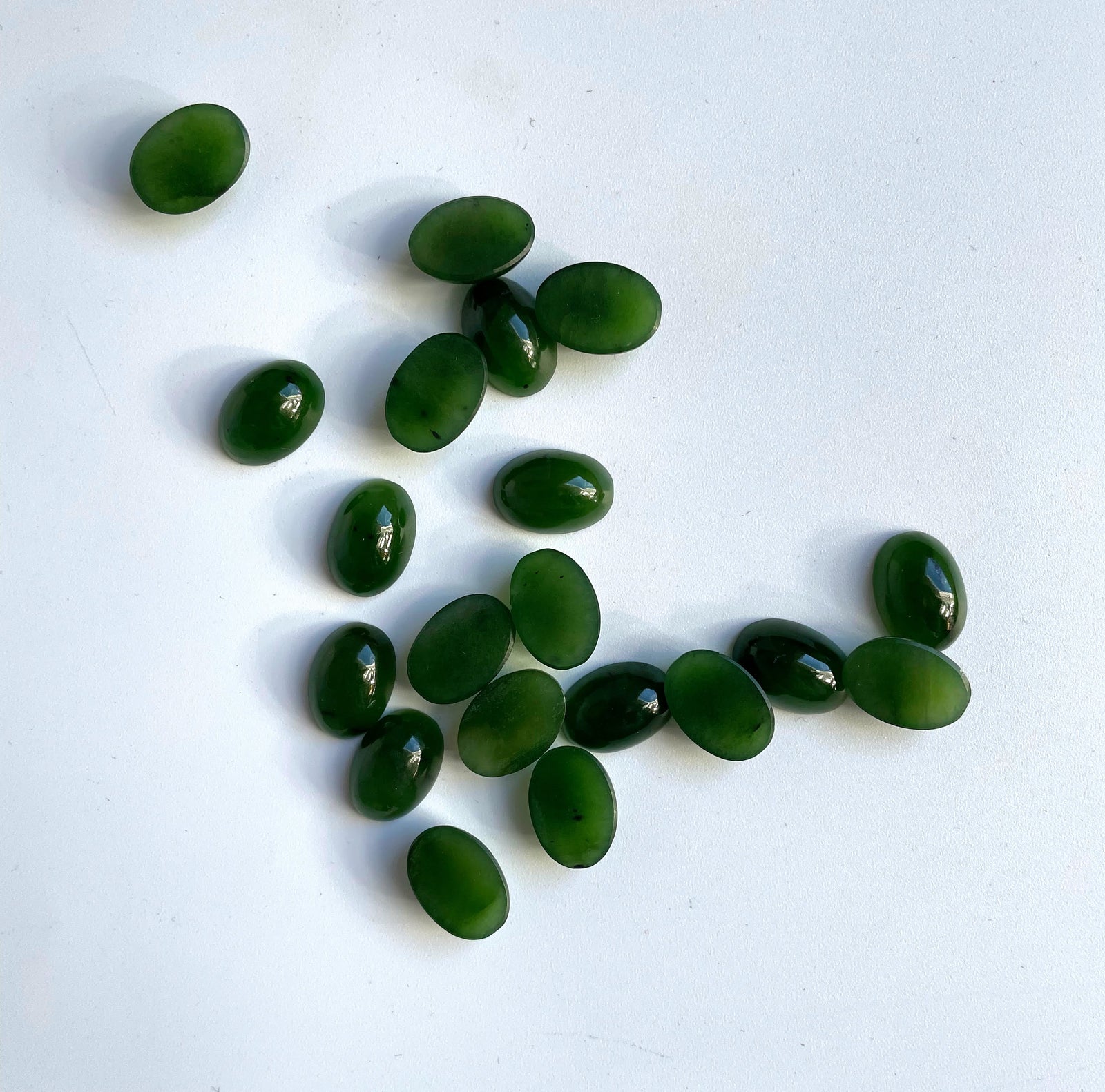 Rich green Siberian jade oval cabochons scattered on a white surface