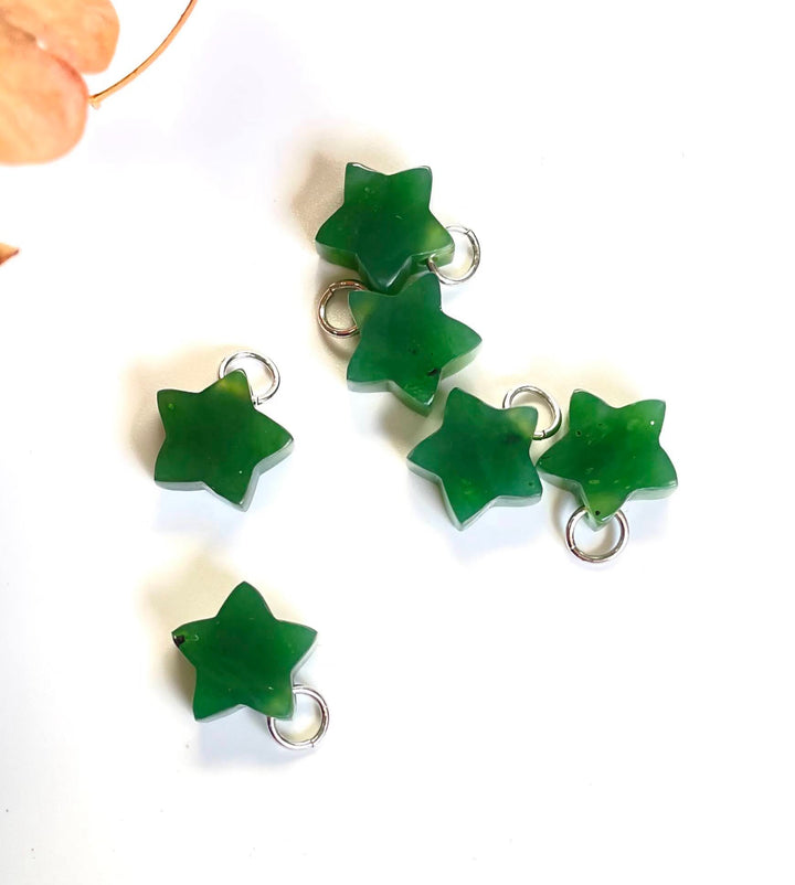Group of green jade star charms with silver rings on a light background.