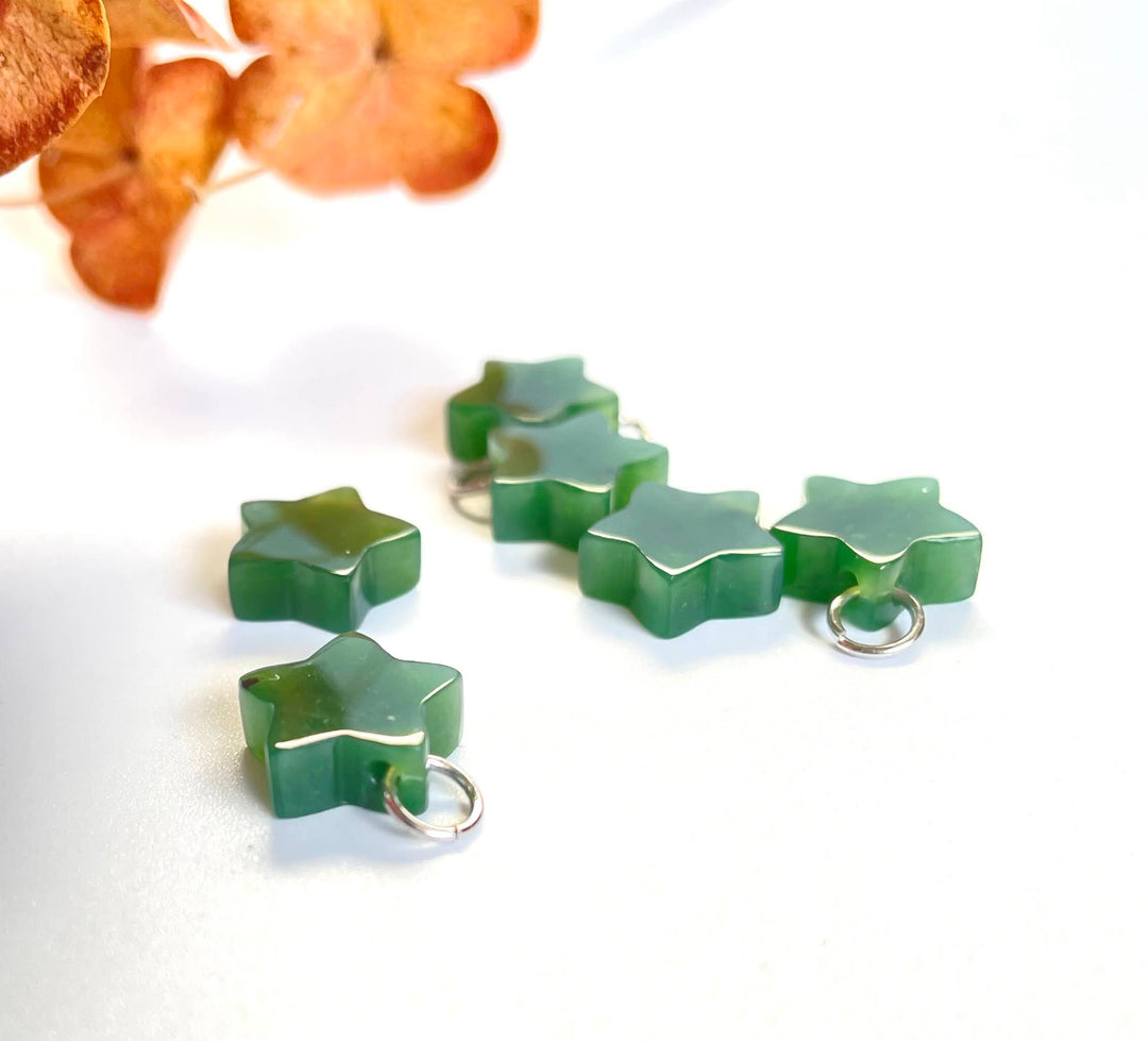 Group of green jade star charms with silver loops on white surface