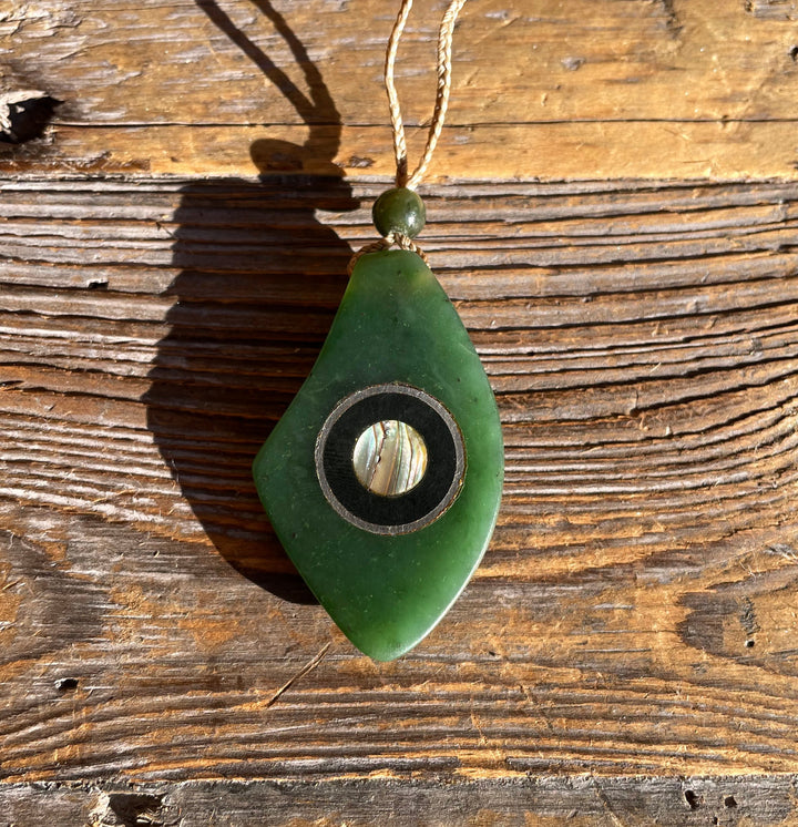 Green jade pendant with circular abalone shell inlay surrounded by a black ring