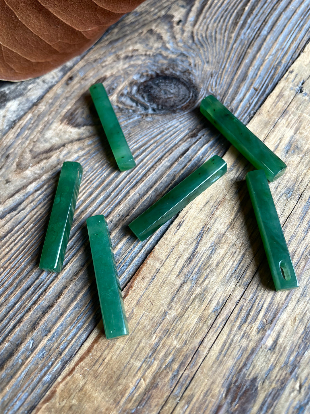 Several green jade rectangular beads scattered on a rustic wooden surface.
