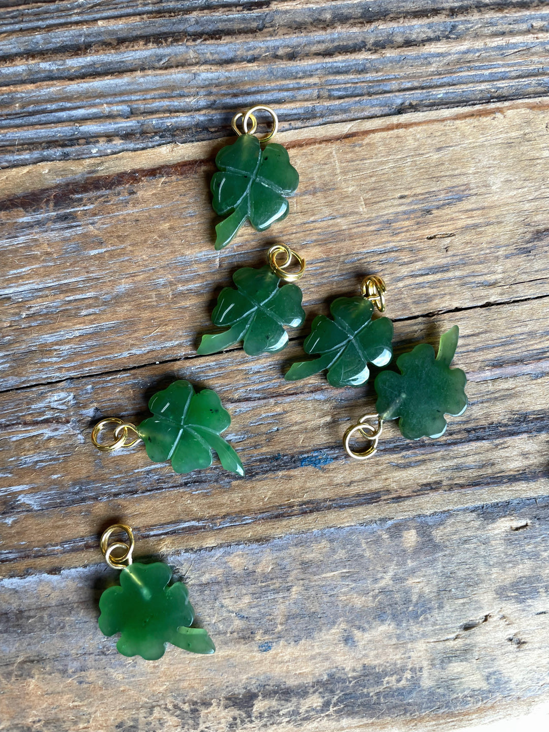 Several green shamrock charms with gold loops laid on rustic wooden surface
