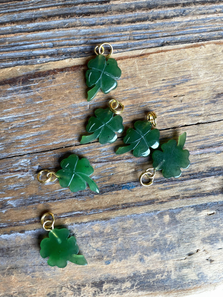 Several green shamrock charms with gold loops laid on rustic wooden surface