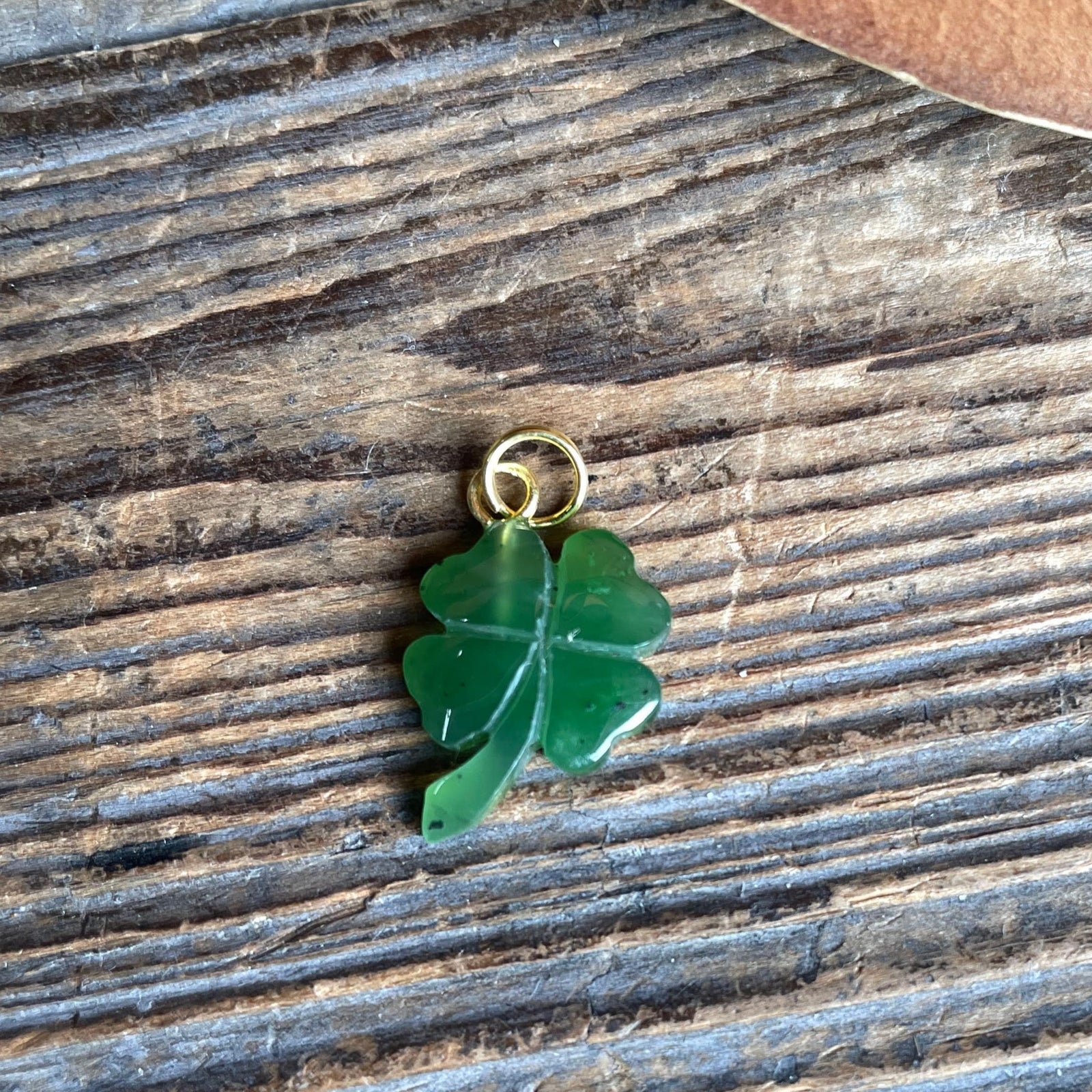 A green jade shamrock charm with a gold loop sits on a rustic wooden surface.